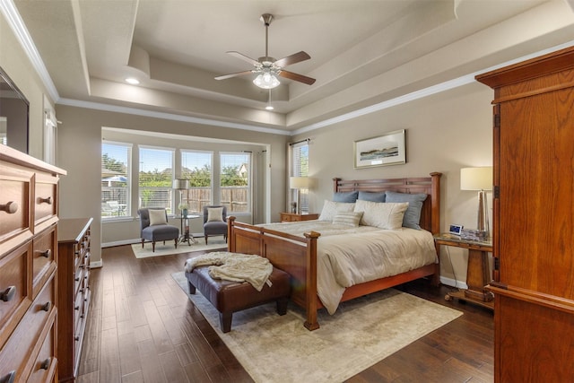 bedroom with a tray ceiling, dark wood finished floors, ornamental molding, ceiling fan, and baseboards