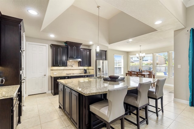 kitchen with appliances with stainless steel finishes, a kitchen breakfast bar, a sink, under cabinet range hood, and backsplash