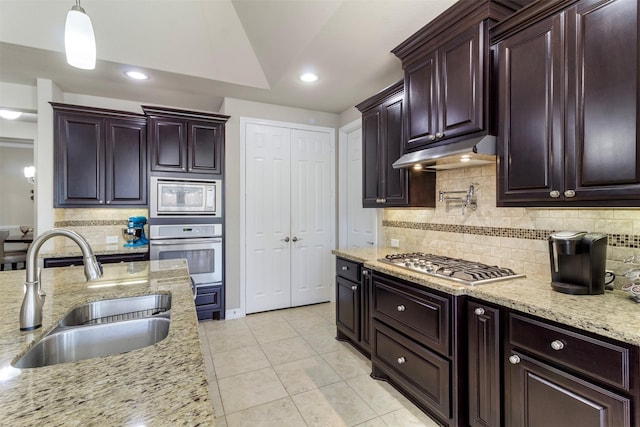 kitchen featuring decorative light fixtures, appliances with stainless steel finishes, a sink, light stone countertops, and under cabinet range hood