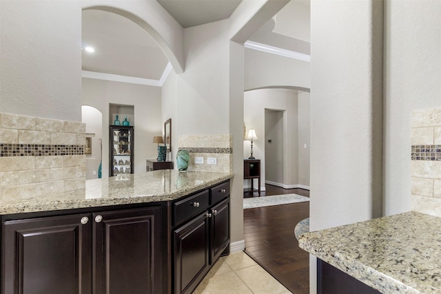 kitchen with light stone countertops, light tile patterned floors, ornamental molding, and decorative backsplash