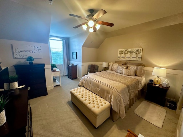 bedroom with a wainscoted wall, ceiling fan, vaulted ceiling, and light colored carpet