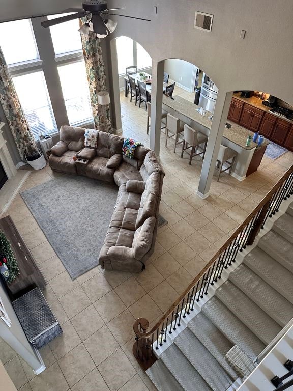 living room featuring arched walkways, a towering ceiling, visible vents, stairs, and a ceiling fan