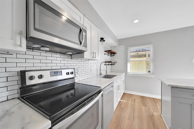 kitchen with light stone counters, stainless steel appliances, tasteful backsplash, light wood-style floors, and a sink