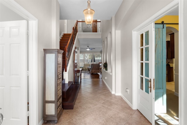 foyer entrance featuring arched walkways, light tile patterned flooring, stairway, and a barn door