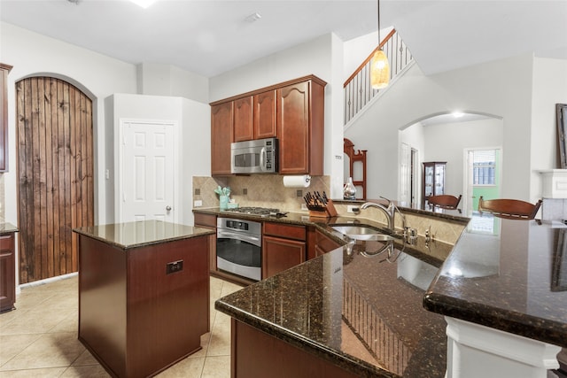 kitchen featuring arched walkways, a kitchen island, a sink, stainless steel appliances, and backsplash