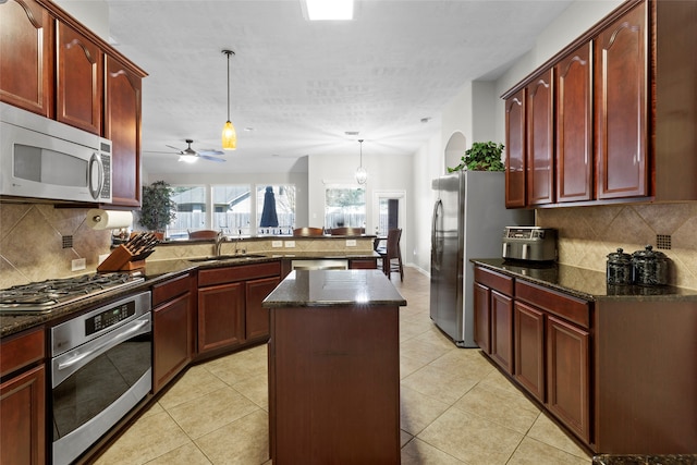 kitchen with light tile patterned floors, appliances with stainless steel finishes, a peninsula, dark brown cabinets, and a sink