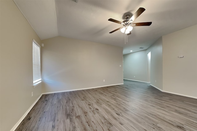 empty room with a ceiling fan, lofted ceiling, baseboards, and wood finished floors