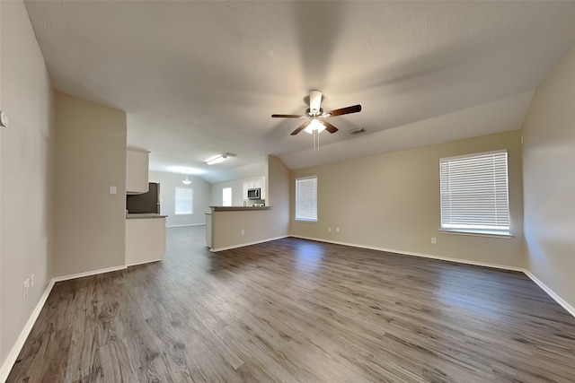 unfurnished living room with lofted ceiling, ceiling fan, dark wood-type flooring, and baseboards