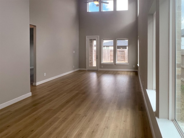 unfurnished living room with plenty of natural light, a high ceiling, baseboards, and wood finished floors