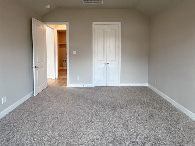 unfurnished bedroom with lofted ceiling, a closet, visible vents, and carpet flooring