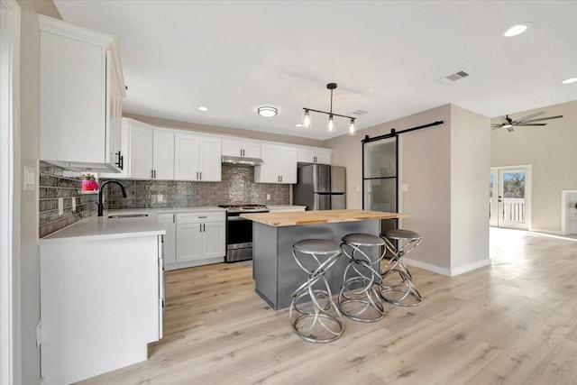 kitchen with a barn door, butcher block countertops, a sink, appliances with stainless steel finishes, and decorative backsplash