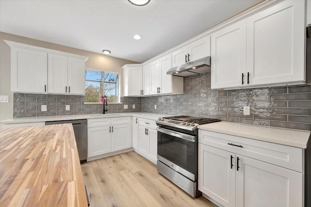 kitchen featuring under cabinet range hood, stainless steel appliances, butcher block countertops, a sink, and light wood finished floors