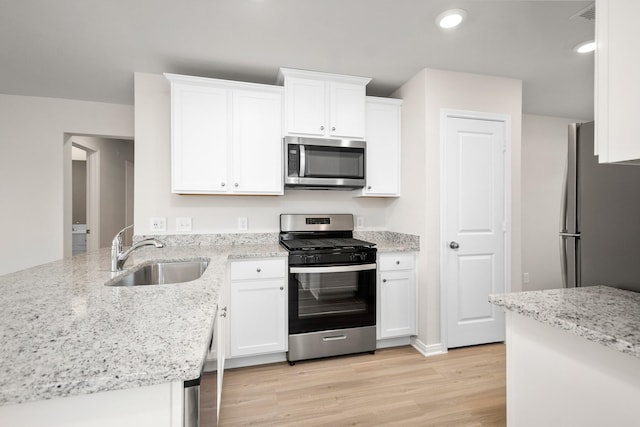 kitchen featuring appliances with stainless steel finishes, light stone counters, light wood-type flooring, white cabinetry, and a sink