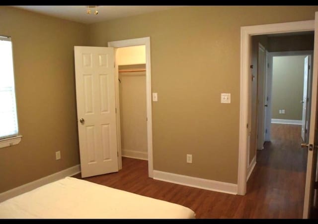 unfurnished bedroom with a spacious closet, a closet, wood finished floors, and baseboards