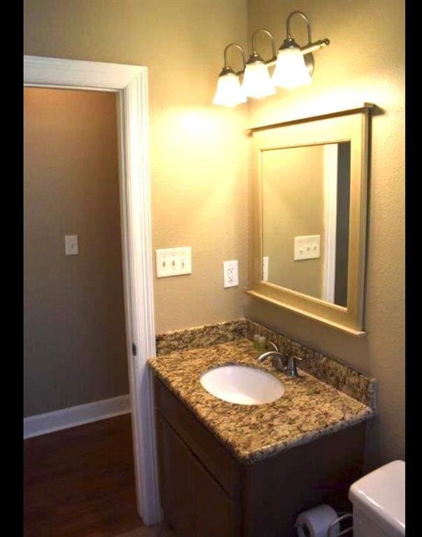 bathroom with toilet, wood finished floors, vanity, and baseboards