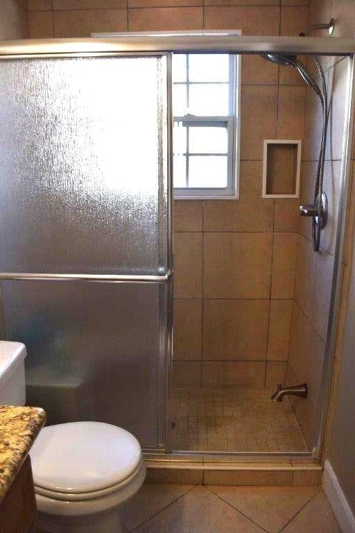 bathroom featuring toilet, a shower stall, and tile patterned flooring