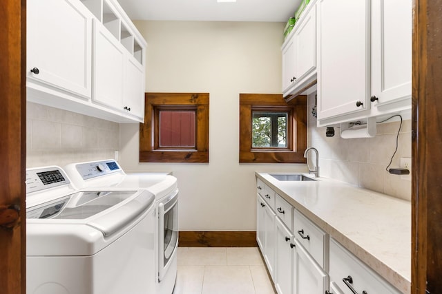 laundry area with light tile patterned floors, separate washer and dryer, a sink, baseboards, and cabinet space