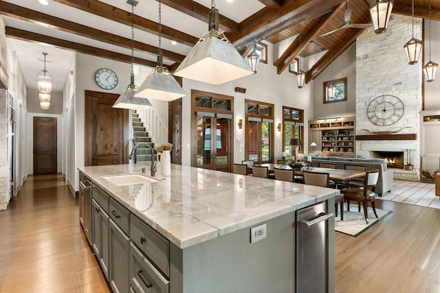 kitchen with a fireplace, gray cabinetry, a kitchen island with sink, a sink, and light wood-type flooring