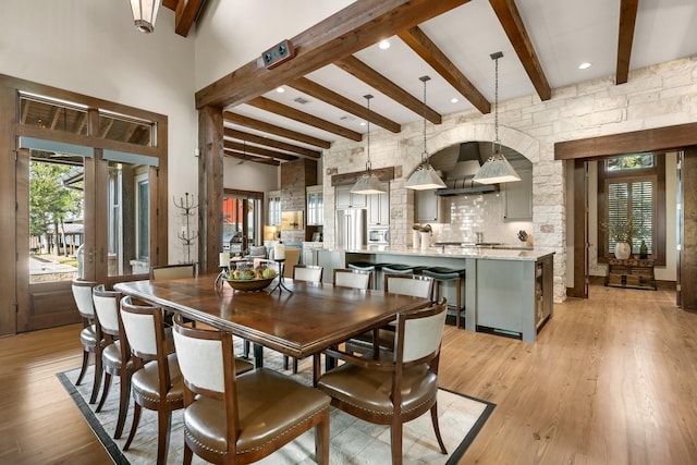 dining room with light wood-type flooring, a high ceiling, and beam ceiling