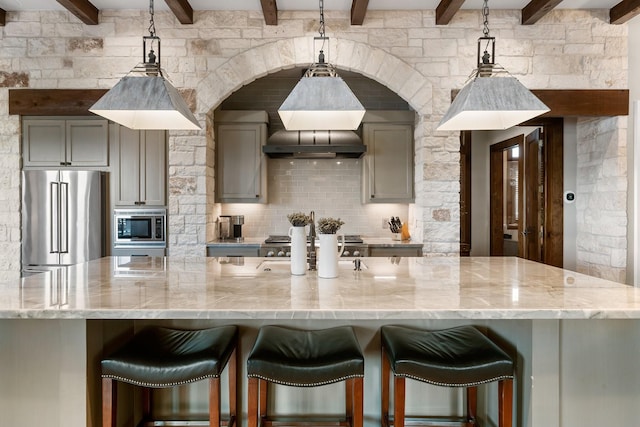 kitchen featuring appliances with stainless steel finishes, beamed ceiling, light stone counters, and gray cabinetry