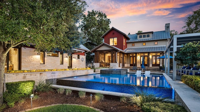 rear view of house featuring a patio, a chimney, metal roof, a standing seam roof, and a pool with connected hot tub