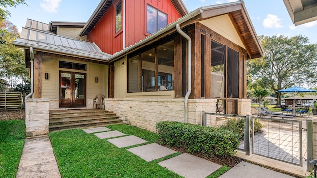 view of front of home with stone siding, a standing seam roof, fence, french doors, and board and batten siding