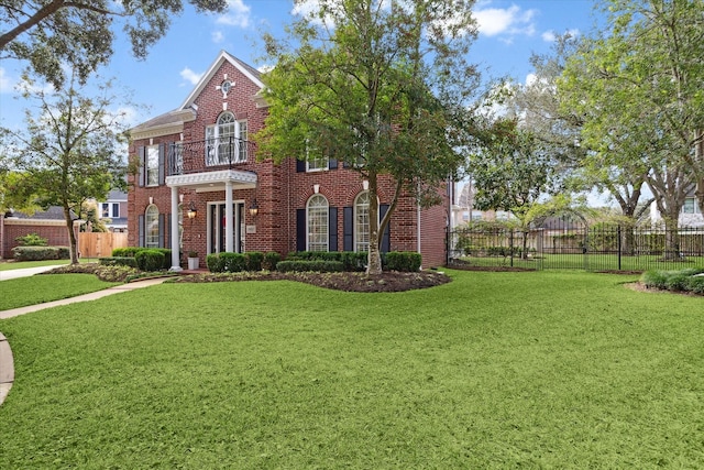 colonial-style house featuring brick siding, a front yard, fence, and a balcony