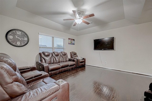 living room featuring a ceiling fan, a tray ceiling, visible vents, and wood finished floors