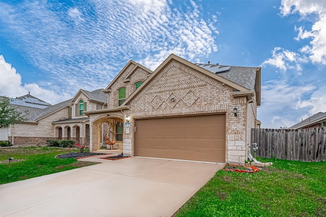 french country inspired facade with brick siding, an attached garage, a front yard, fence, and driveway