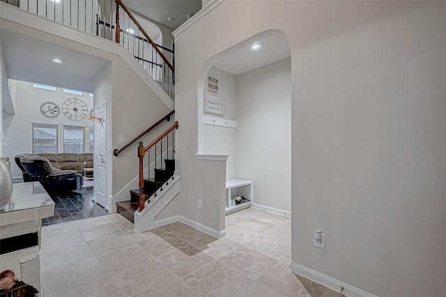 stairway with arched walkways, a high ceiling, recessed lighting, and baseboards