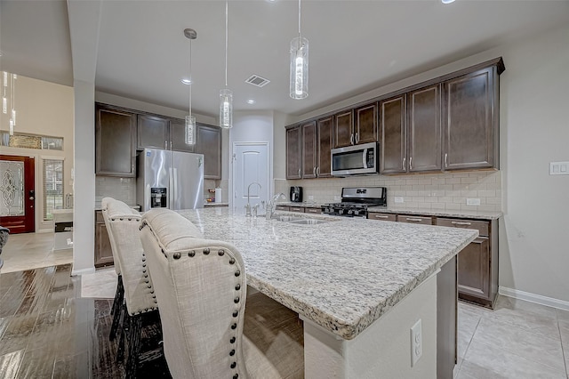 kitchen with appliances with stainless steel finishes, a sink, dark brown cabinets, and light stone countertops