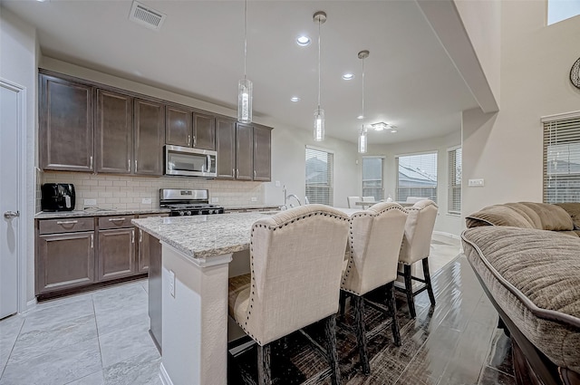 kitchen featuring visible vents, open floor plan, dark brown cabinets, appliances with stainless steel finishes, and decorative backsplash