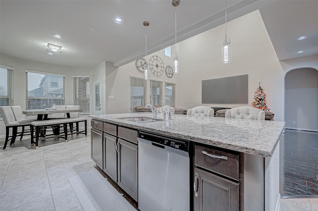 kitchen featuring arched walkways, a sink, open floor plan, stainless steel dishwasher, and light stone countertops