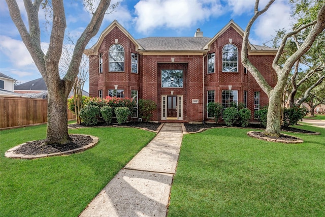 view of front of house with brick siding, a shingled roof, a chimney, fence, and a front yard