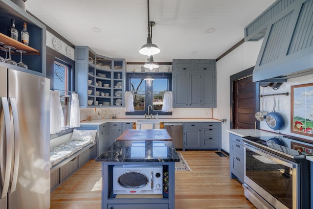 kitchen with appliances with stainless steel finishes, dark stone countertops, light wood-type flooring, open shelves, and a sink