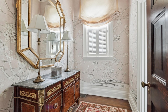 interior space featuring wallpapered walls, baseboards, wood finished floors, and vanity