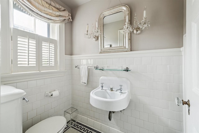 half bath featuring wainscoting, a sink, toilet, and tile walls