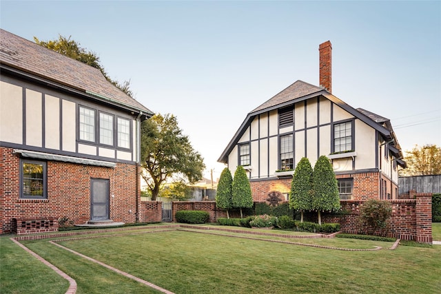 exterior space featuring brick siding, a lawn, a chimney, fence, and stucco siding