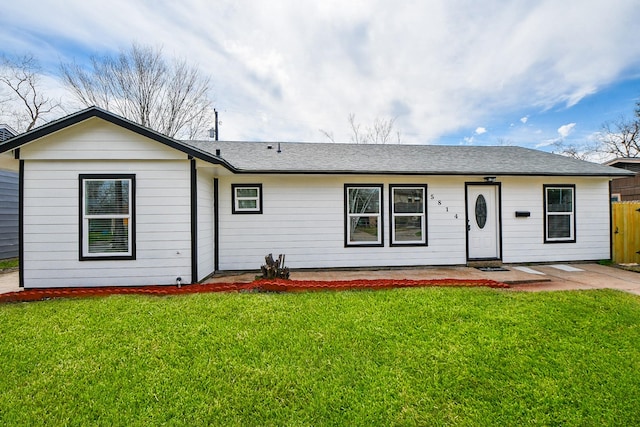 view of front of house with a patio, roof with shingles, a front yard, and fence