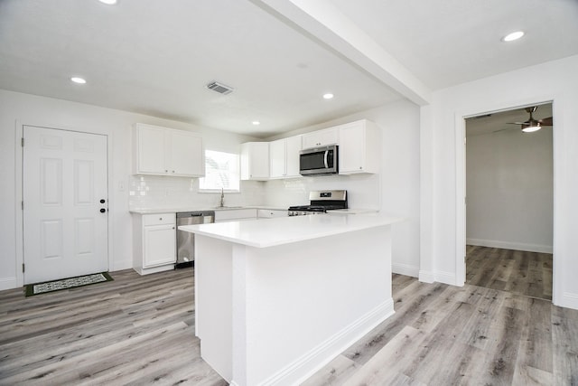 kitchen featuring light wood finished floors, stainless steel appliances, tasteful backsplash, visible vents, and white cabinets