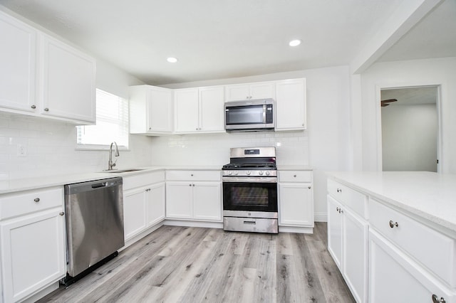 kitchen with stainless steel appliances, a sink, white cabinets, and light wood-style floors