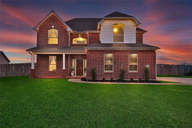 traditional-style house featuring a front lawn, roof with shingles, fence, and brick siding