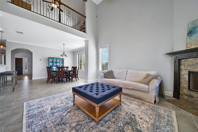 tiled living area with arched walkways, crown molding, a fireplace, visible vents, and baseboards