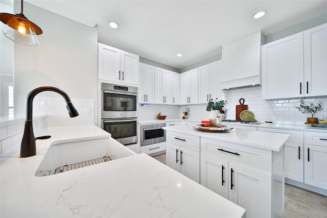 kitchen with custom exhaust hood, white cabinetry, appliances with stainless steel finishes, and a sink