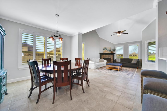 dining room featuring ceiling fan with notable chandelier, a fireplace, baseboards, vaulted ceiling, and crown molding