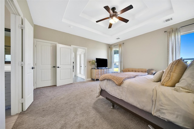 bedroom with multiple windows, visible vents, a raised ceiling, and light colored carpet