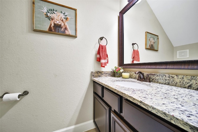 bathroom featuring a textured wall, visible vents, vaulted ceiling, and vanity