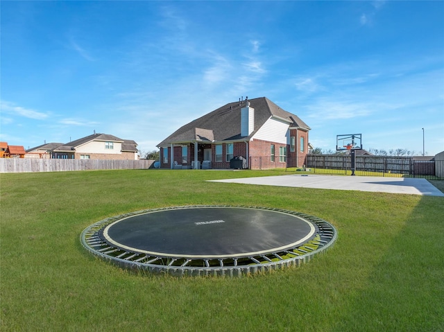 view of yard with community basketball court, a trampoline, and fence