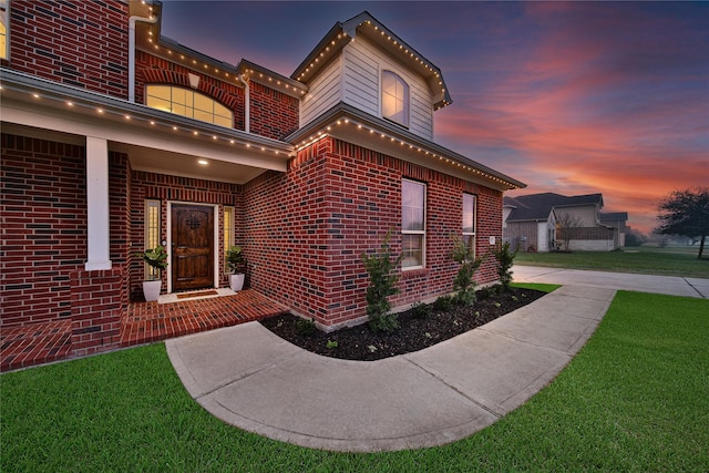 exterior entry at dusk with a balcony, a lawn, and brick siding