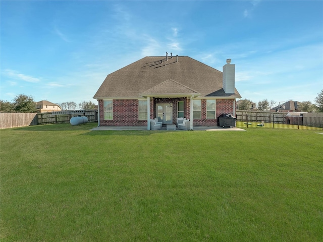 rear view of house with brick siding, a lawn, a chimney, and a fenced backyard